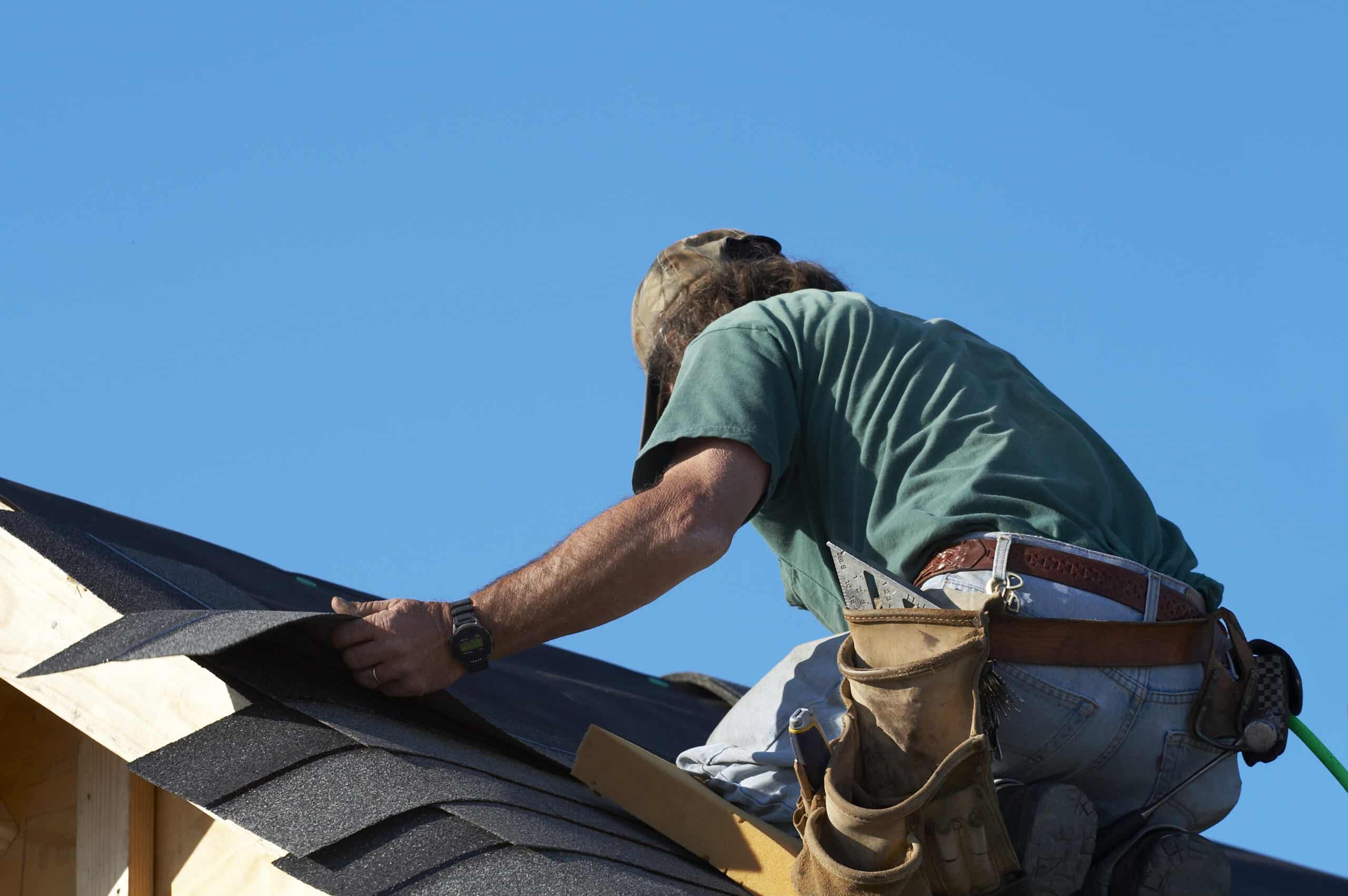 worker on roof putting shingles down